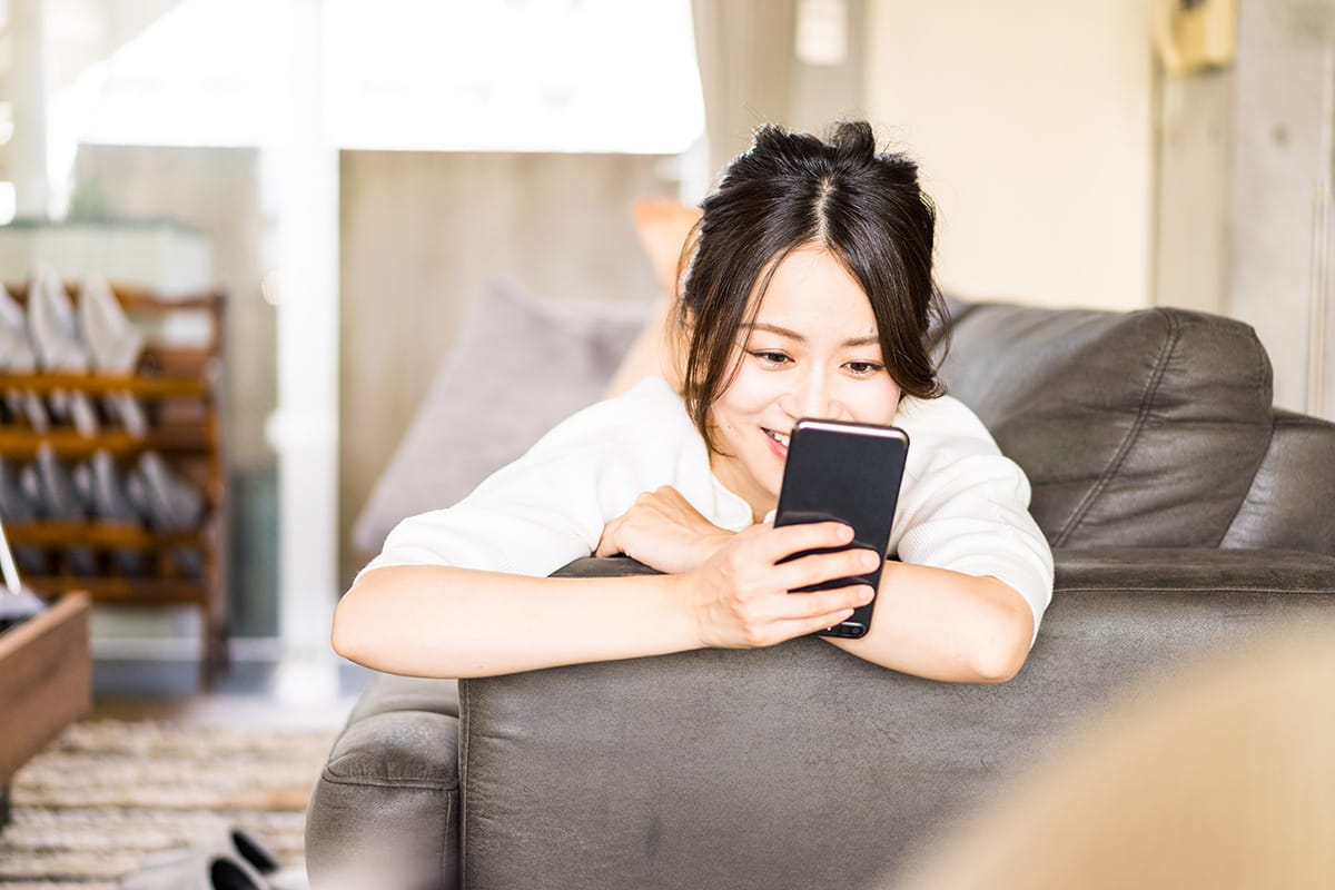 ソファで横になってスマートフォンを操作する女性